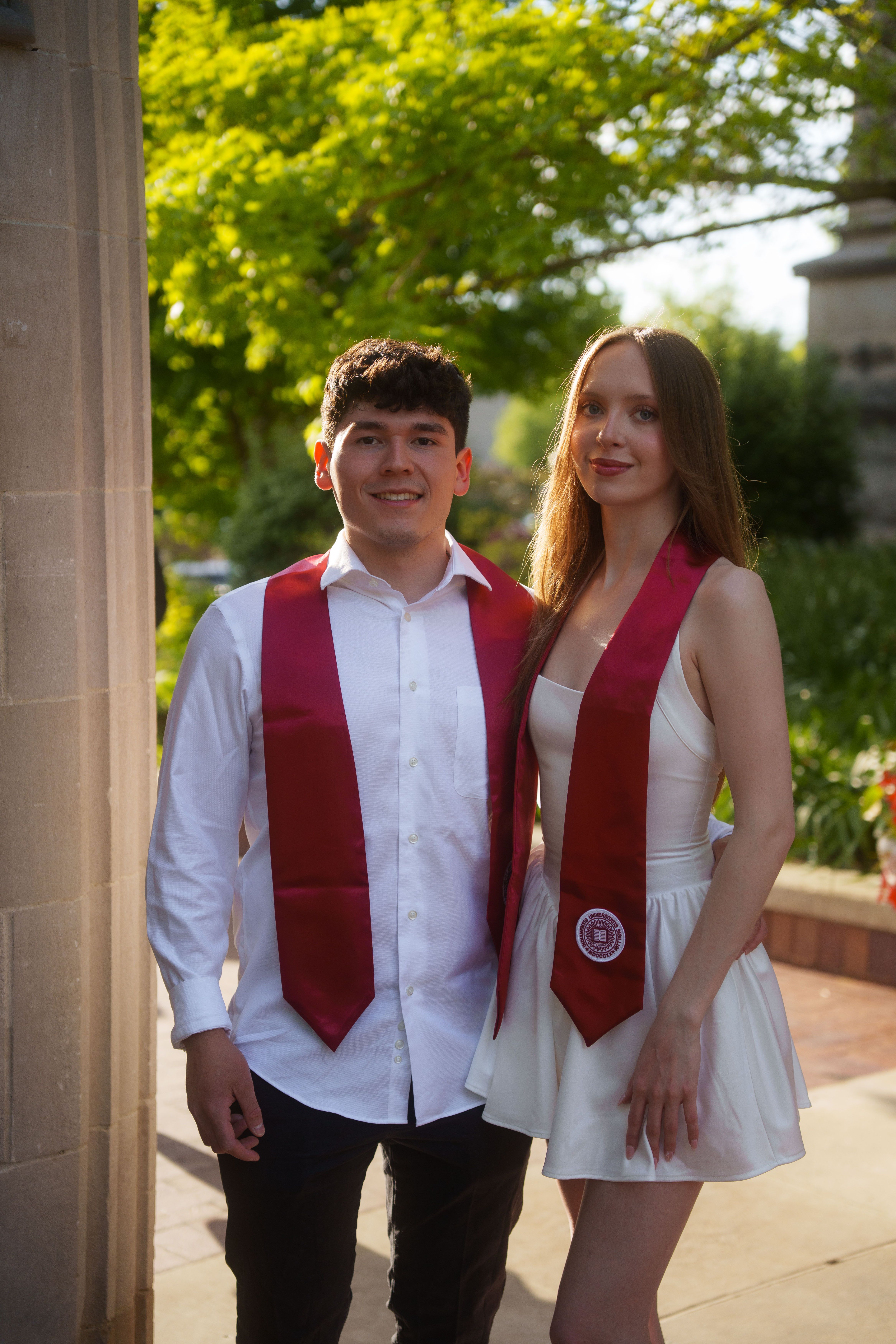Three graduates in white dresses at sunset.