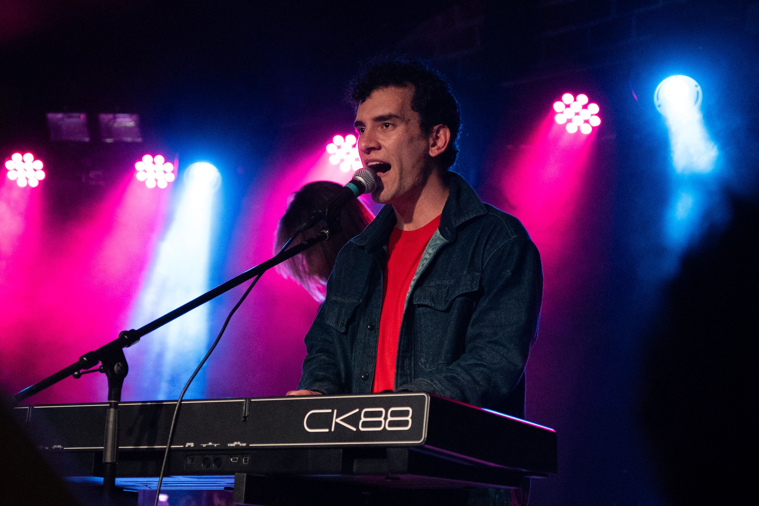 A keyboardist in a navy jacket singing while looking ahead.