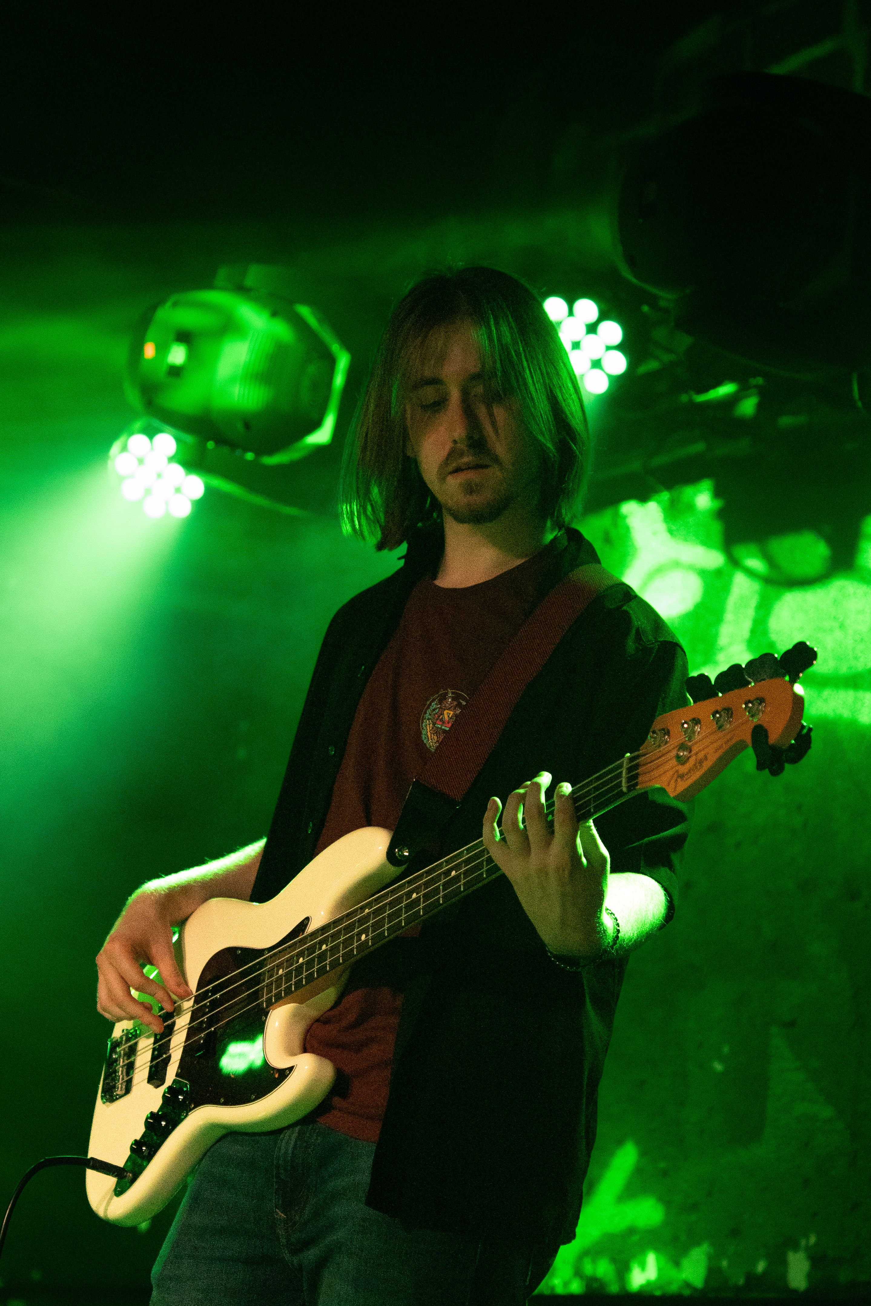 Bass guitarist playing a white Fender with green lighting behind him.